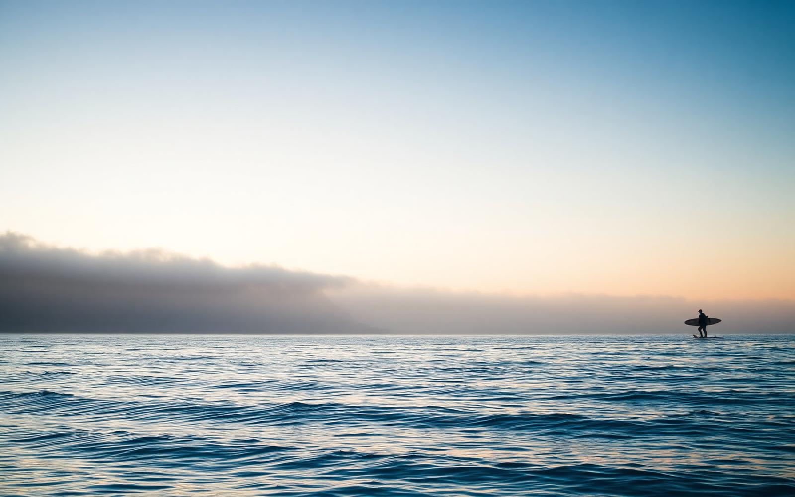 Lone surfer paddling on glassy ocean at dawn
